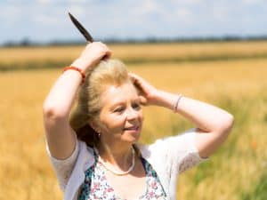 Eine Frau steht an einem Getreidefeld und steckt sich eine Feder ins Haar.