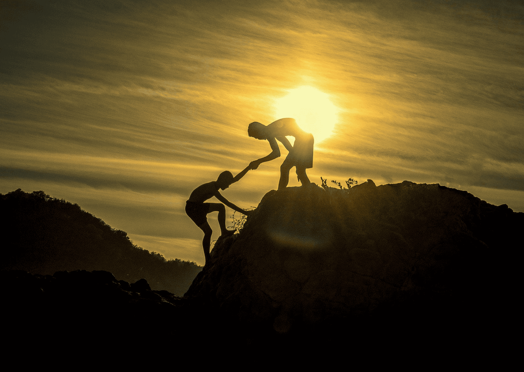 Podcast-Folge 10 – Es gibt viele Arten zu helfen - Es ist eine Berglandschaft bei Sonnenuntergang steht eine Person auf einem Berg und reicht einer anderen Person die Hand, um ihr auf den Gipfel zu helfen.
