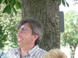 Ein Mann mit hochgeschobener Sonnenbrille sitzt an einen Baum gelehnt.
