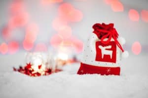 Ein rotweißes Säckchen steht im künstlichen Schnee und im HIntergrund ist ein kleines Glas mit einer Kerze zu sehen, das umgeben ist von roten Sternen.