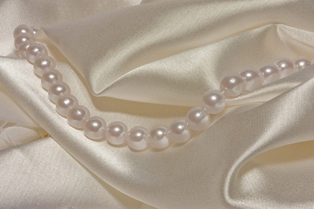 Auf einem seidigen Stofff liegt eine Perlenkette.