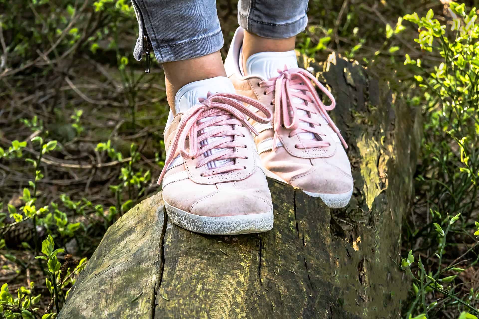 Es sind zwei Füße in rosafarbenen Sneakers auf einem Baumstamm zu sehen.