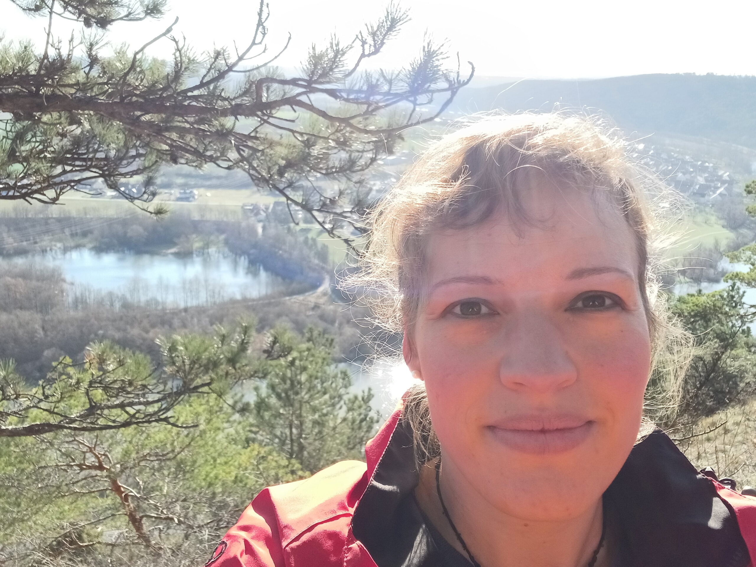 Feedback "Erinnere Dich an Deine Heilkraft" Stephanie Rockenmaier Eine Frau schaut lächelnd in die Kamera und in ihrem Rücken ist eine Landschaft mit einem See